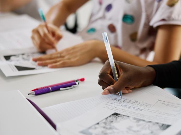 Hands of two students writing notes on paper